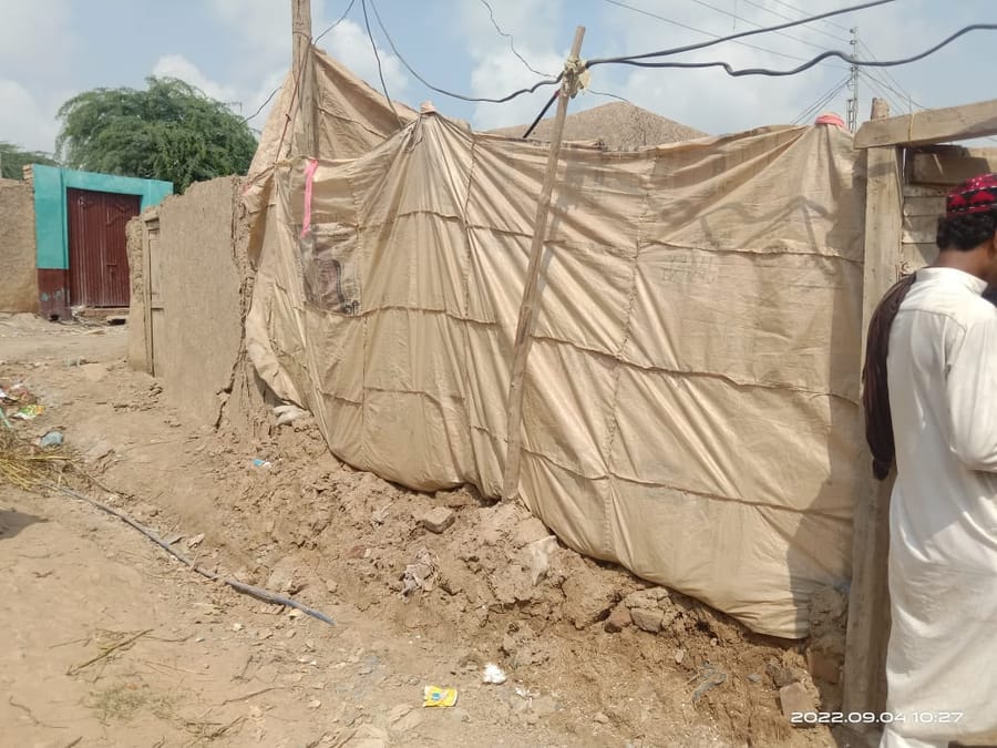A tarpaulin shelter beside a flood-damaged compound